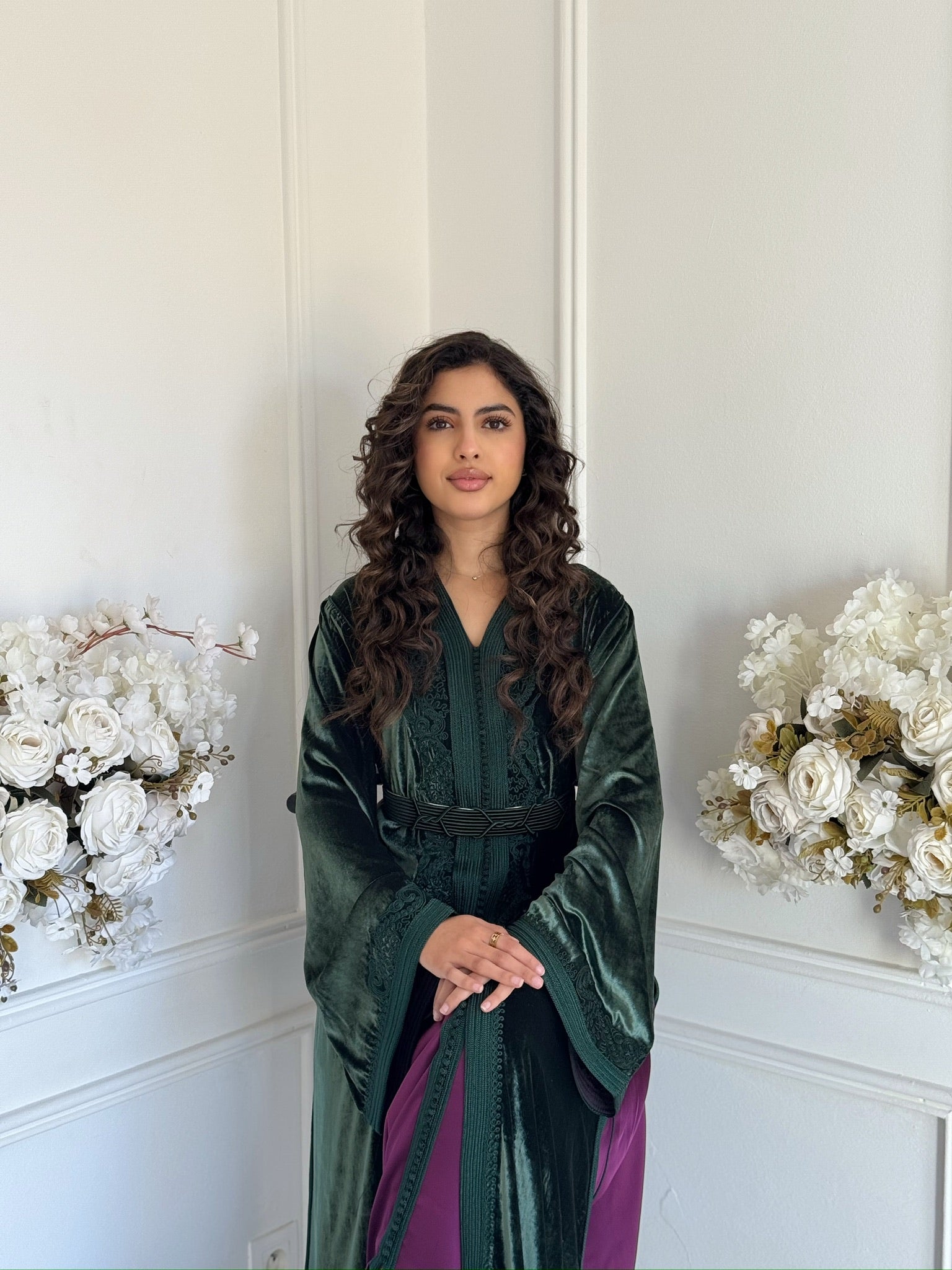 “Dark green velvet Moroccan caftan with purple details displayed in an elegant interior with white floral decor