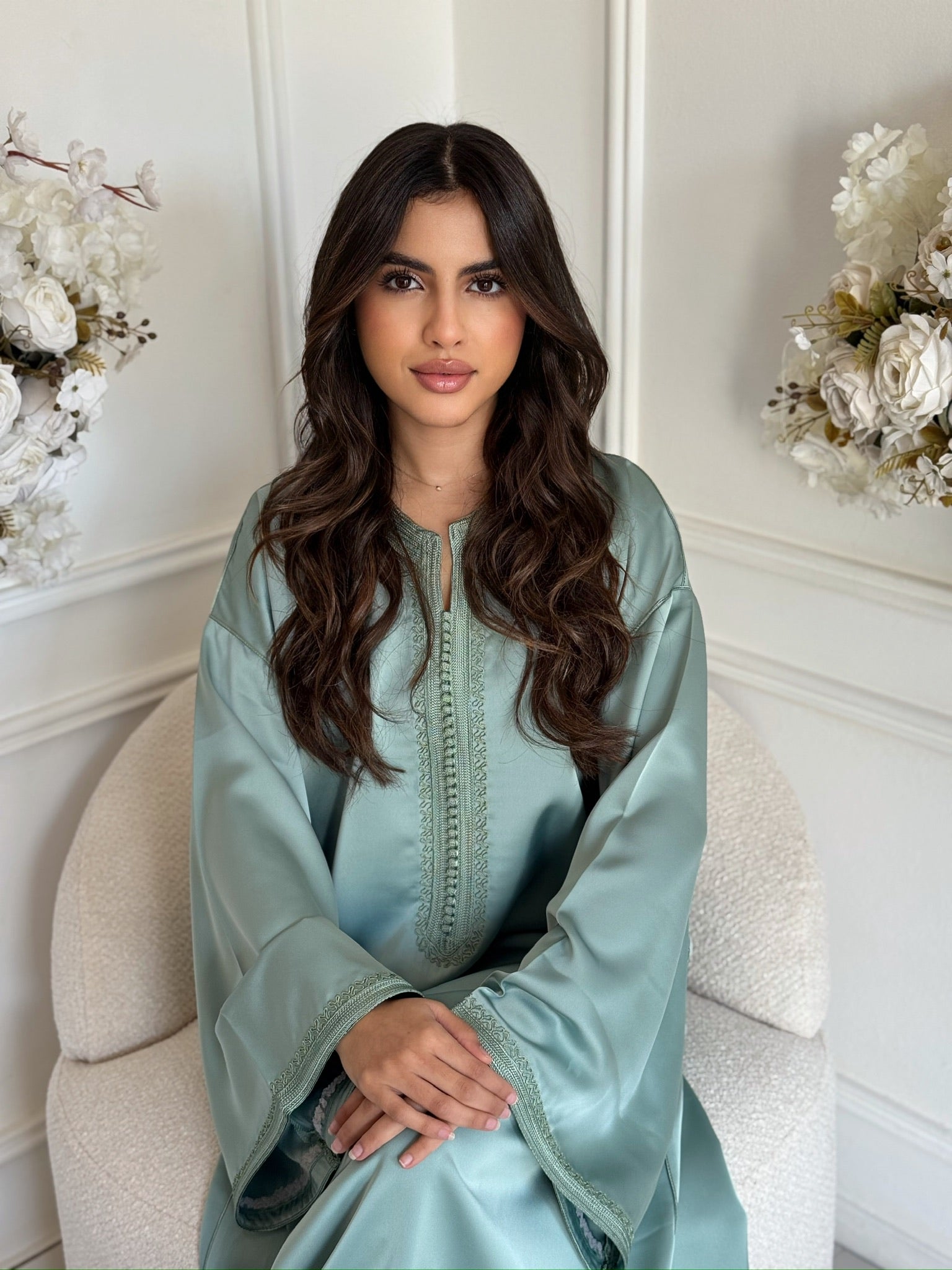 Model wearing a mint green Moroccan gandoura sitting with floral décor in a bright room