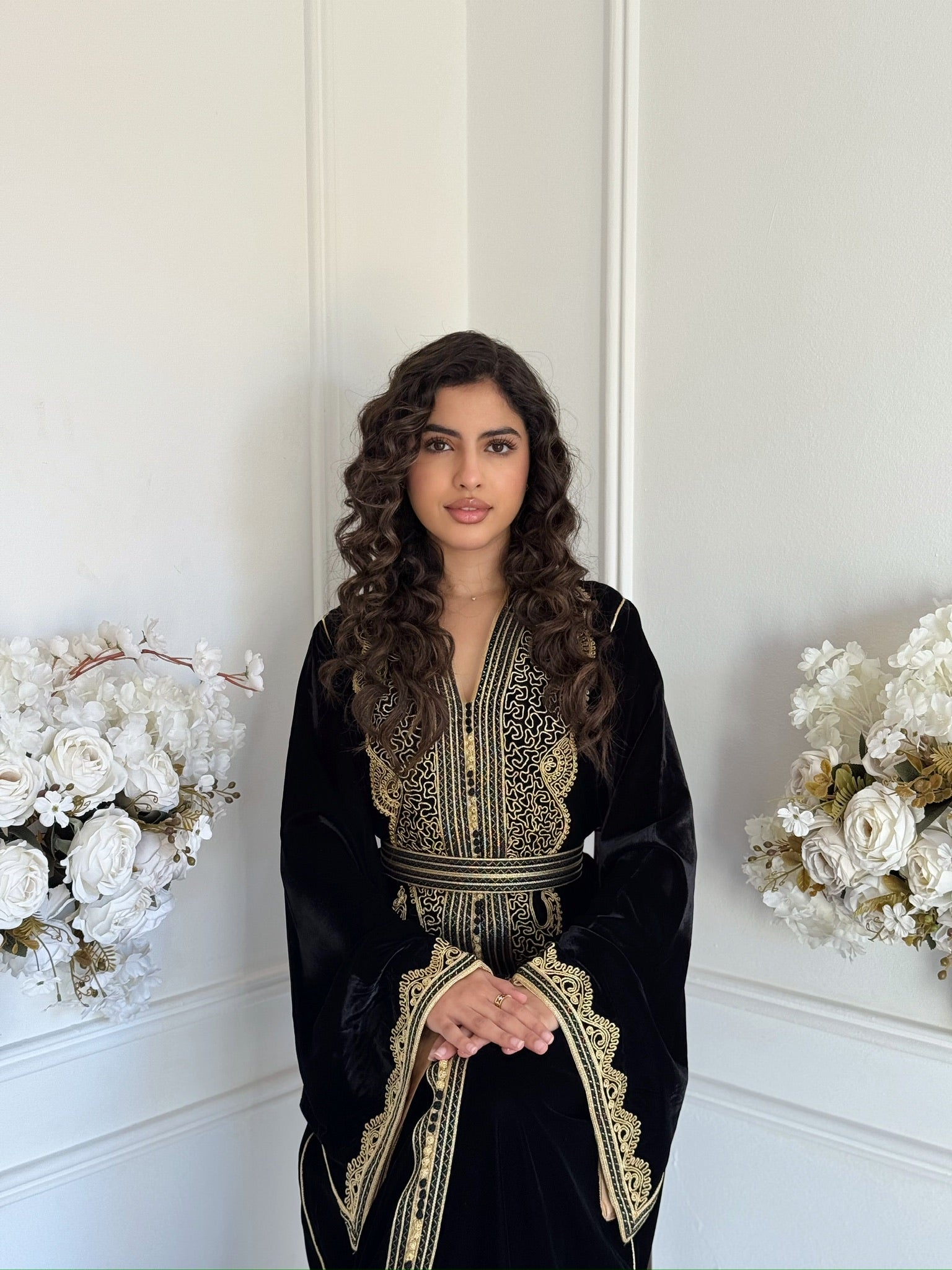 Black and gold luxury Moroccan caftan by Mobra displayed in an elegant interior with white floral decor.