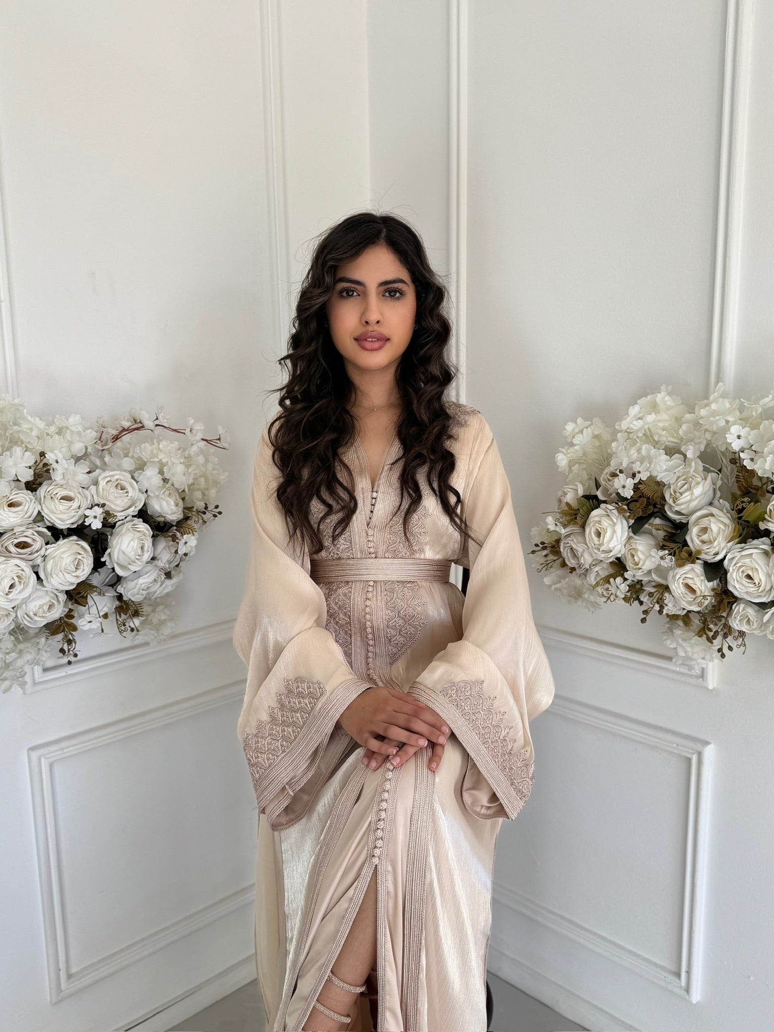 Soft pink organza Moroccan takchita with elegant embroidery displayed in a refined floral interior.”