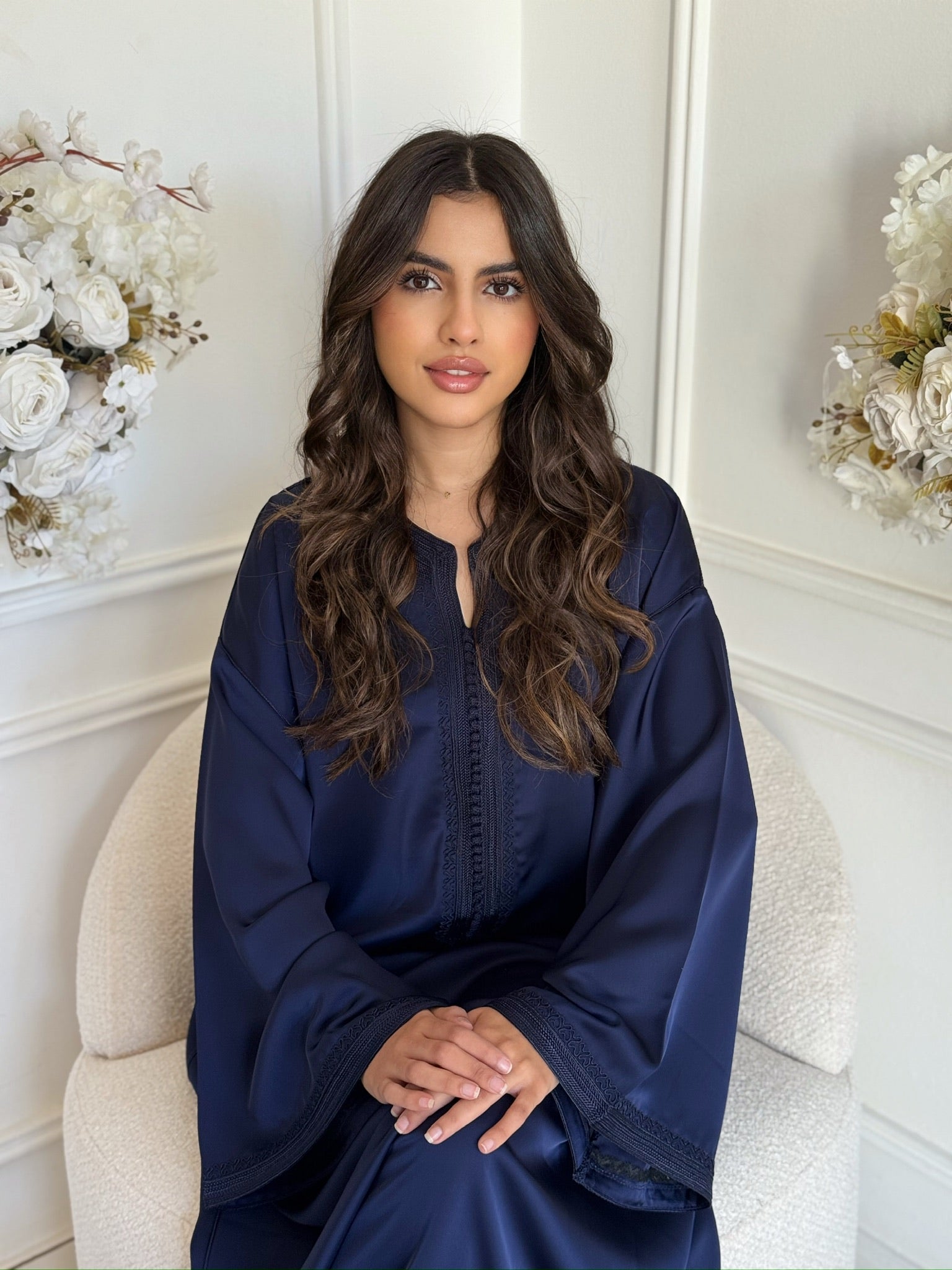 Model wearing a navy Moroccan gandoura with elegant embroidery, seated indoors