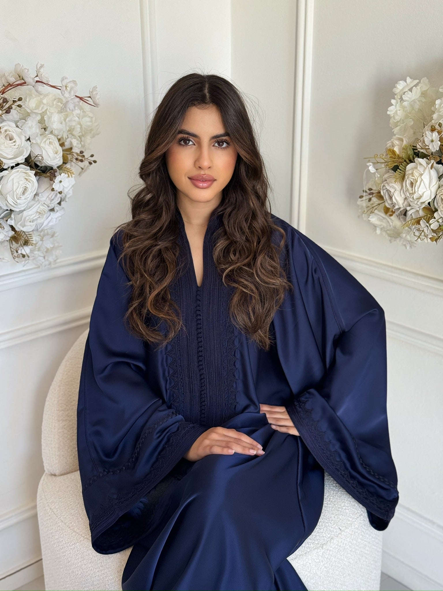 Model wearing a navy blue Moroccan gandoura seated indoors with floral décor
